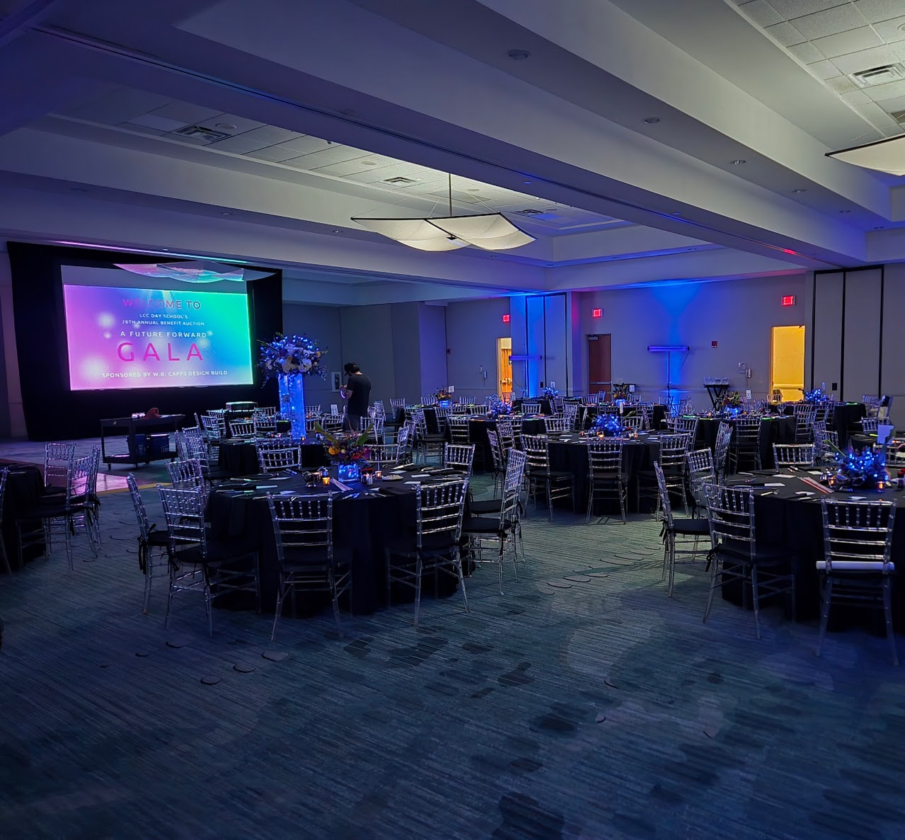Gala ballroom setup with round tables, blue lighting, and projection screen