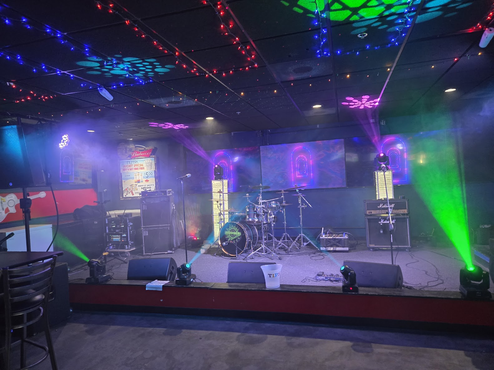 Live music stage with drum kit, PA, and colored event lighting